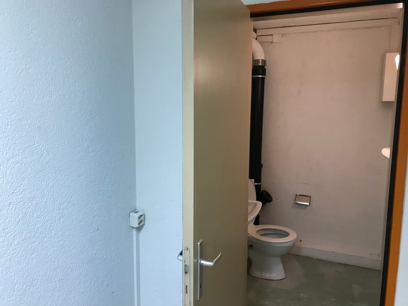 The image shows a bathroom with a toilet, a small space, and a door leading to the room.