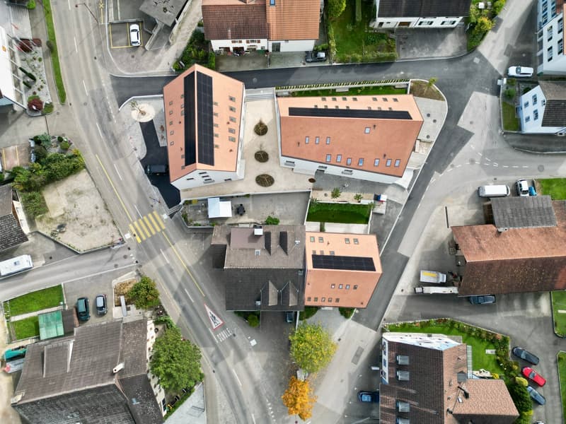 Several residential buildings at a corner, surrounded by streets, driveways, and parking areas. One building has solar panels.