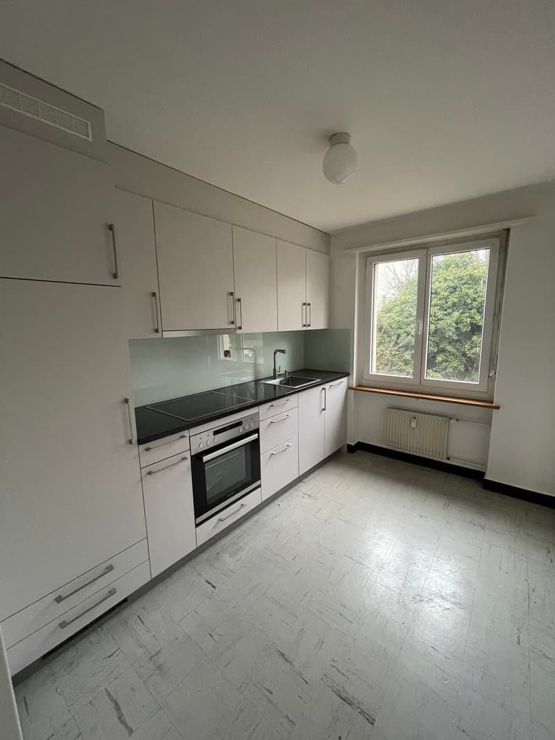 empty modern kitchen, black counter, white cabinets, white drawers, glass window, white floor