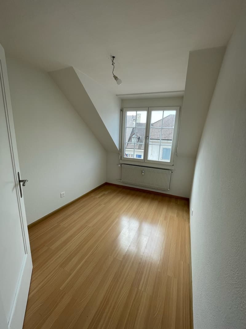 The image shows a bedroom with white walls, a hardwood floor, and a single window. The room appears to be empty, with no furniture or decor visible.