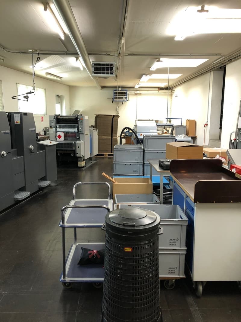 warehouse with industrial machines, storage boxes, shelves, trash bin, and carts