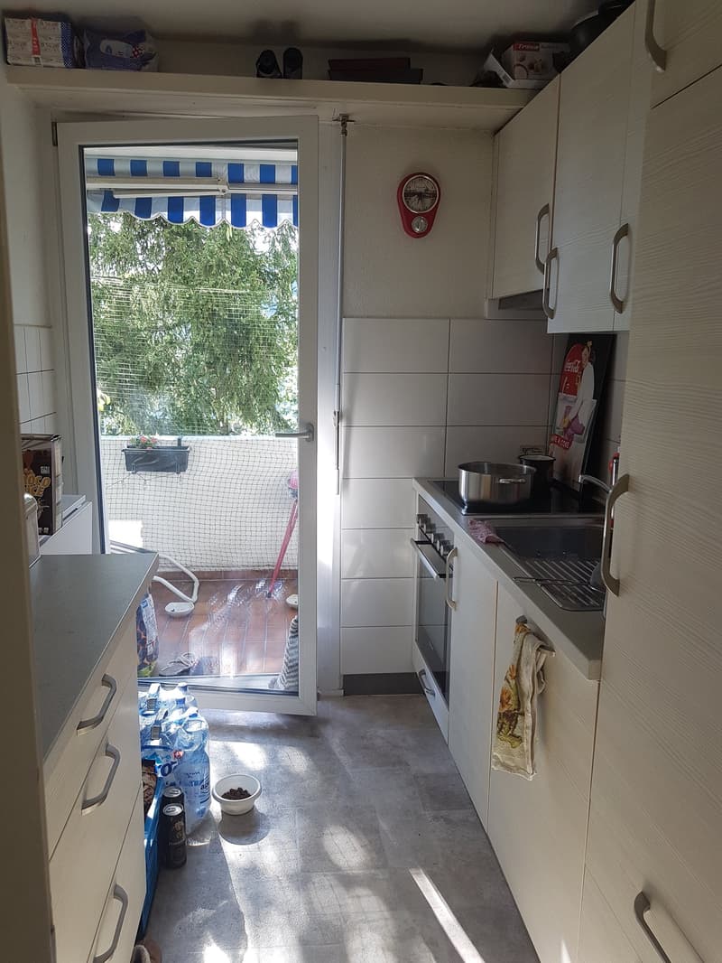 white cabinets, white countertop, open door to balcony, white tile wall, open oven, sink with faucet, light colored floor