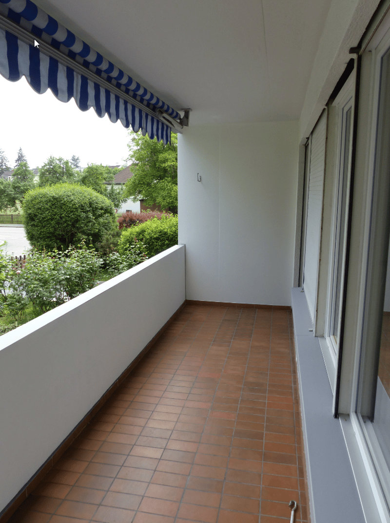 Empty balcony with awning, red floor tiles, closed window