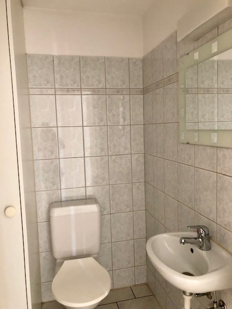 A small bathroom with tile walls, white sink, toilet, mirror, and a faucet