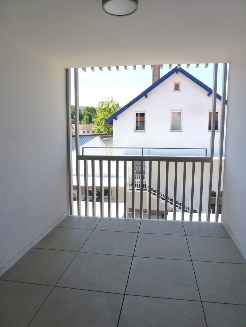 Empty balcony with tiled floor, metal railing, and a view of a house with a blue roof