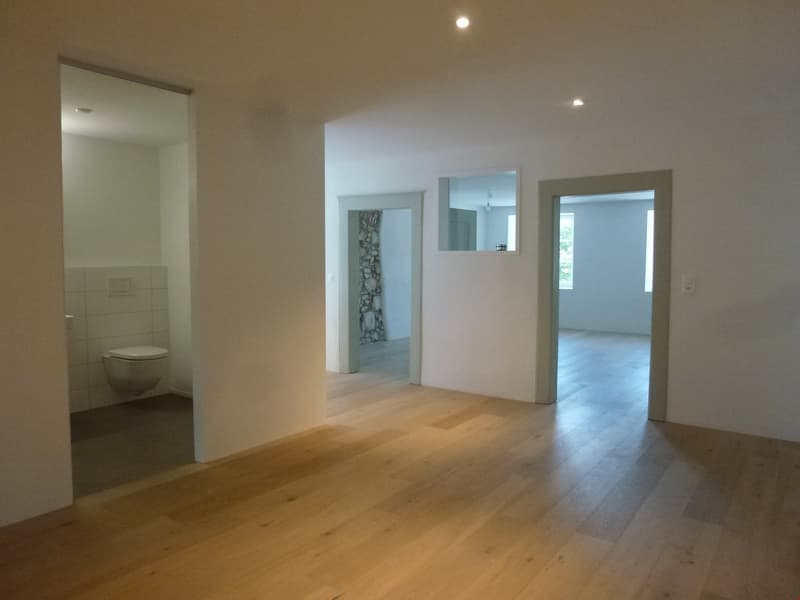 Empty room, wooden floor, white walls, two doors, one leading to a bathroom