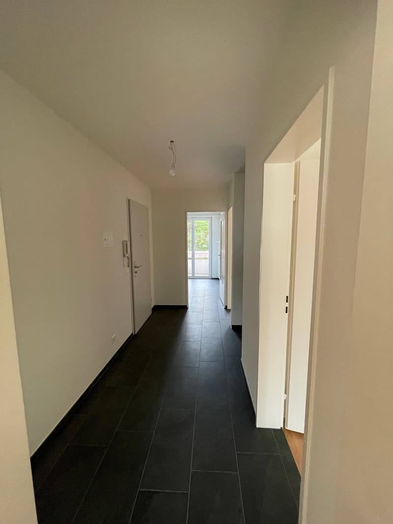 Empty hallway with black tiles, white walls, doors, and a balcony