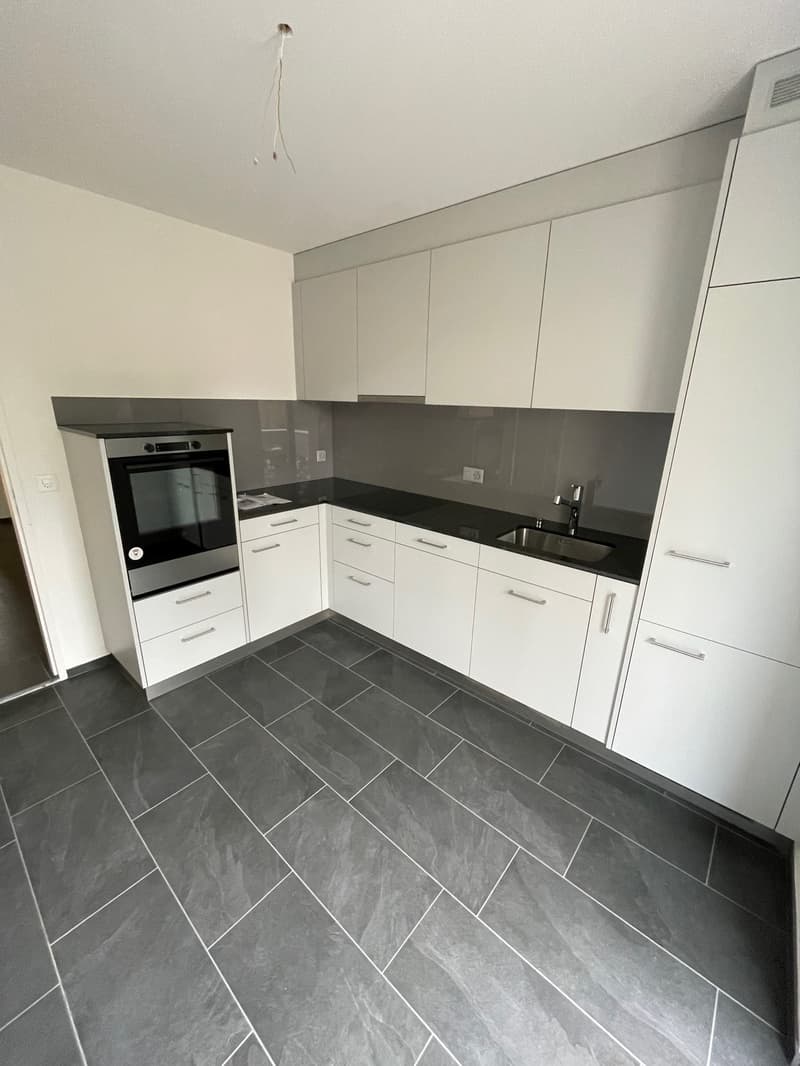 modern kitchen with white cabinets, black countertops, stainless steel oven, sink, faucet, tiled floor