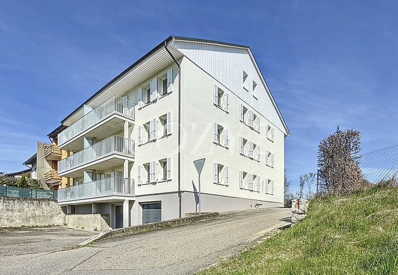 3-story apartment building with white exterior, balconies on each floor, and a paved driveway leading up to the building.