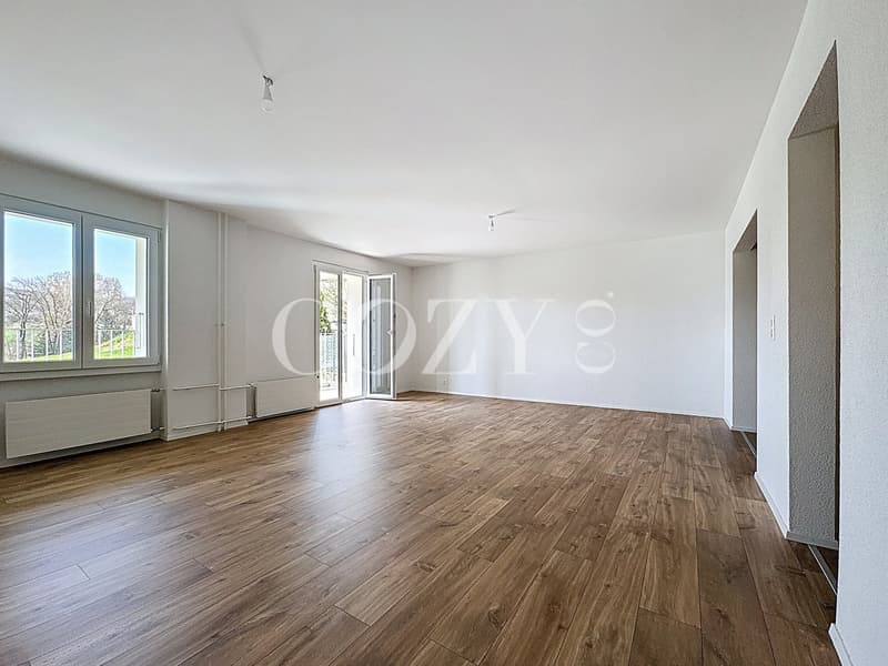 Spacious living room with large windows, hardwood flooring, and a neutral color scheme.