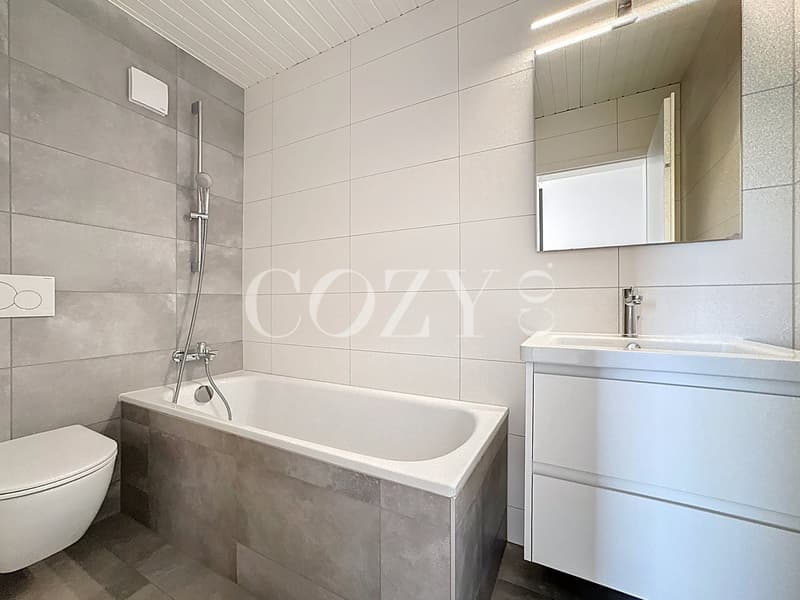 Bathroom with white tiled walls, a bathtub, a vanity with a sink, and a mirror above it.