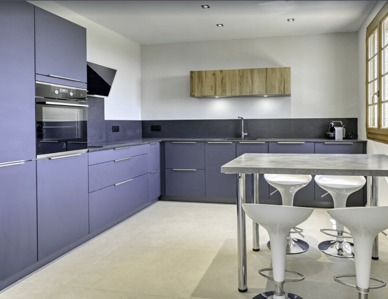 modern kitchen, gray cabinets, black counter top, gas oven, built-in hood, silver refrigerator, kitchen island with stools