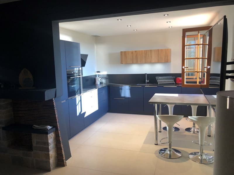 modern kitchen with blue cabinetry, black granite countertop, stainless steel oven, dishwasher, sink, and bar stools under an island with a table, a fireplace, and a door leading to an outdoor view