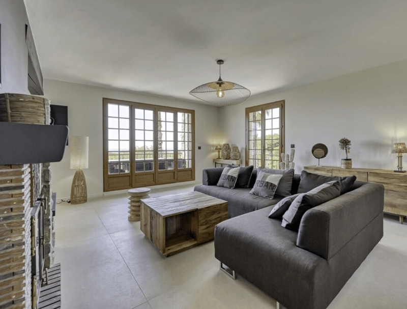 fireplace, large windows, wooden coffee table, gray sofas with pillows, decorative lamps, carpet