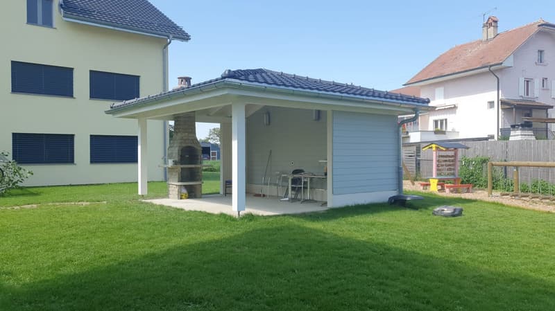outdoor shed with fireplace and tables, near a large grassy yard, two buildings in background