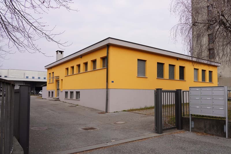 2-story building with yellow exterior, gray wall, multiple windows, garage entrance, letter boxes