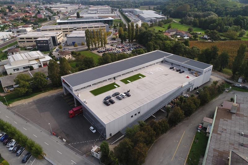 Industrial building, white, solar panels on roof, numerous cars parked in front and on the roof