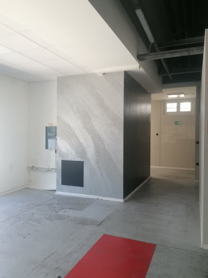 Empty room with white walls, gray floor, large marble wall, red rug, and a window.