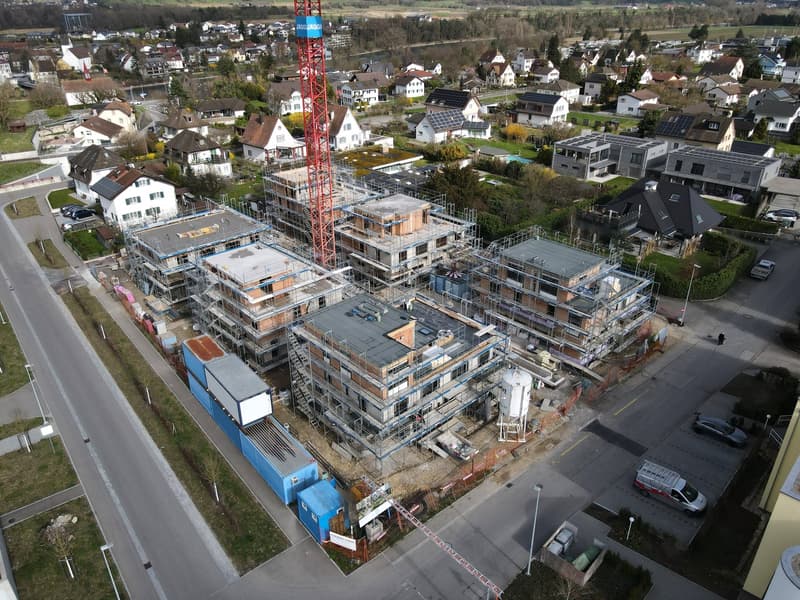Aerial view of a residential area with several houses under construction, featuring a mix of architectural styles, some with solar panels, and a central construction site with a tall crane.