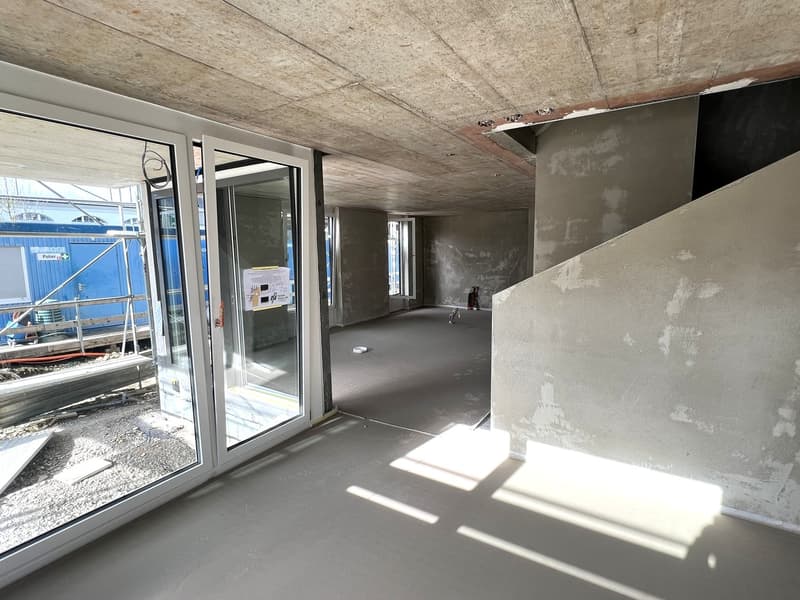 Empty room with glass doors, concrete floor, unfinished walls, construction materials visible