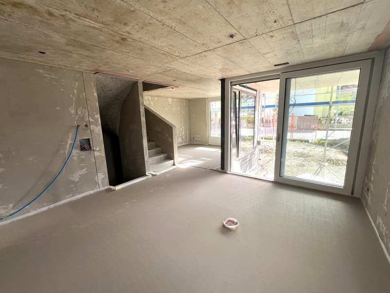 Empty room with concrete floor, unfinished walls, staircase, sliding glass door, and a small bowl on the floor.