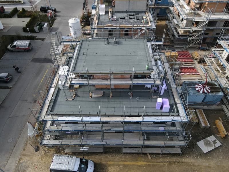Aerial view of a house under construction with scaffolding, grey roof, and multiple levels.