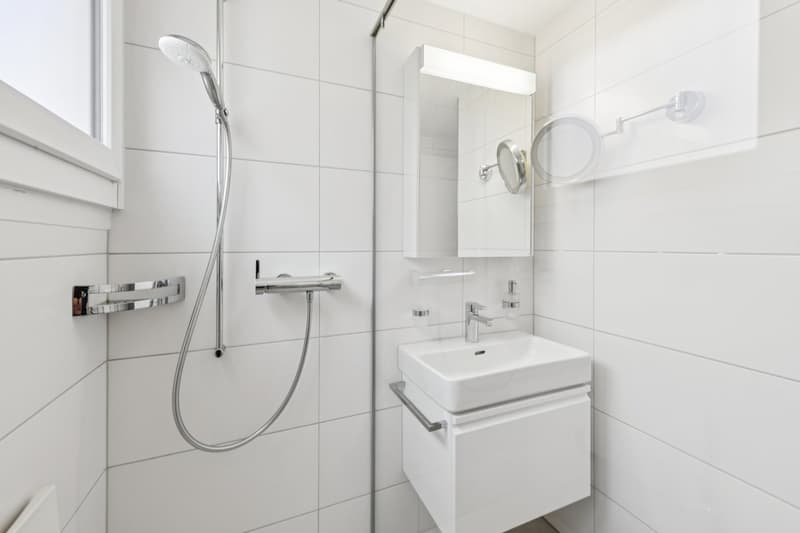 modern bathroom with white tiles, shower, sink, mirror, and a window