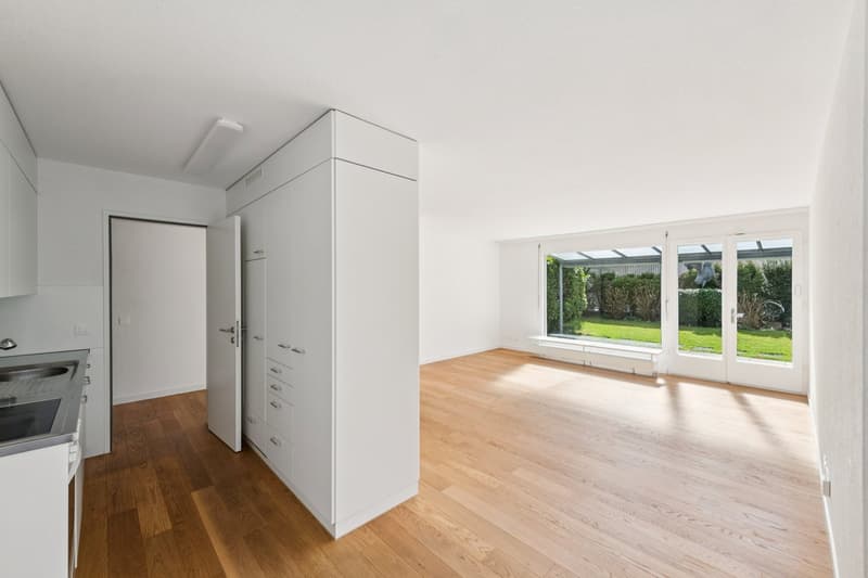 empty room, wooden floor, white walls, large windows, kitchen area with sink and stove
