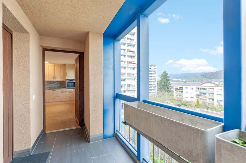 Balcony with blue railings, wooden floor, kitchen with cabinets and microwave, view of the city