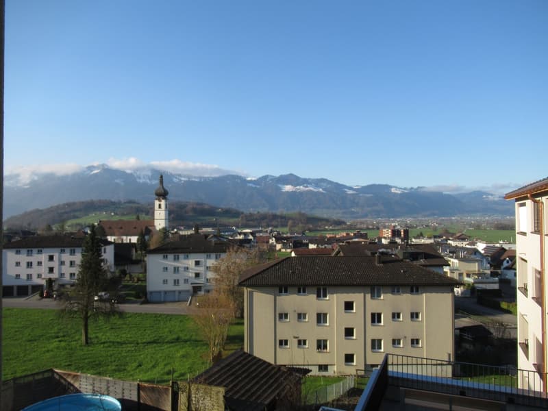 Aerial view of a town with several buildings, mountains in the background, and a clear blue sky.