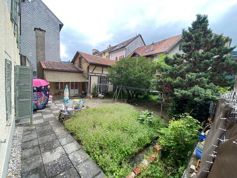 Small garden with a table and chairs, umbrella, and a small canopy. There are trees and plants in the garden.