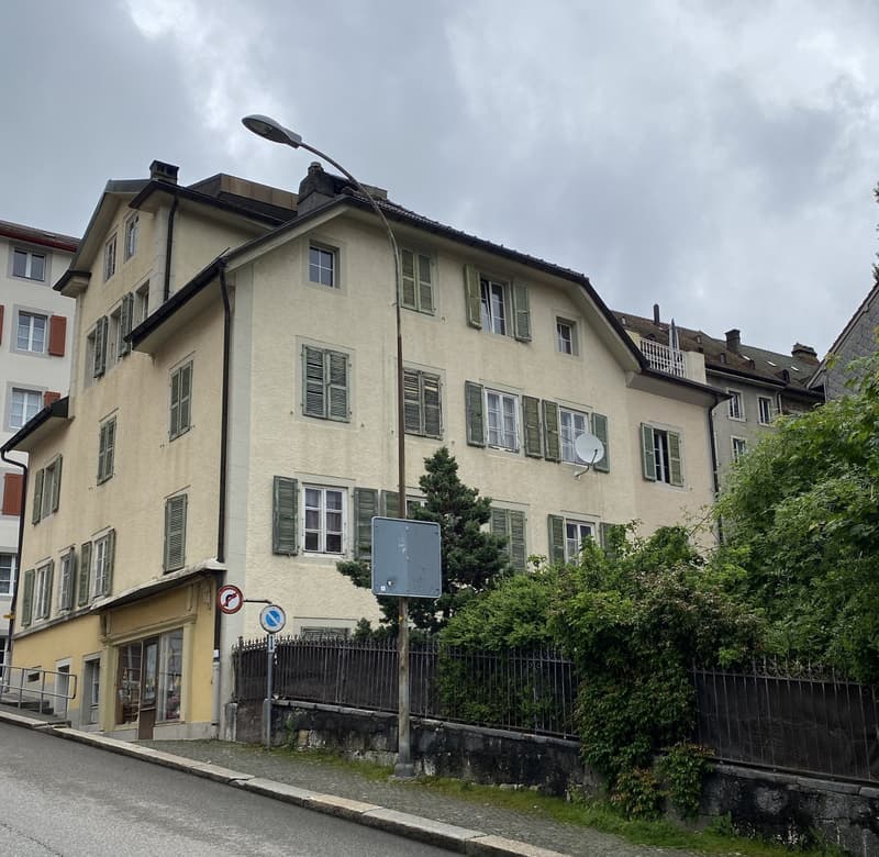 3 story building, beige exterior, multiple windows, green shutters, street light, fence, plants