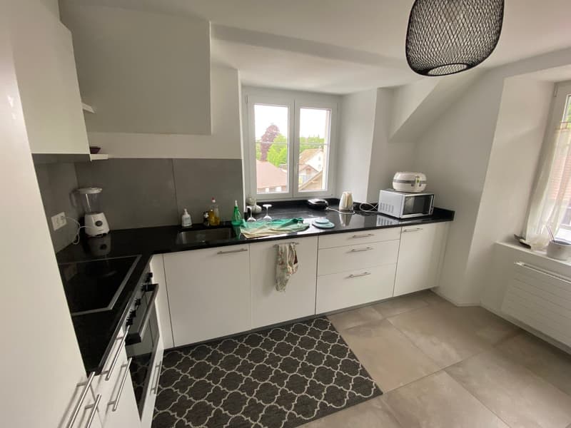 modern kitchen with white cabinets, black countertops, white tiled floor, window with view