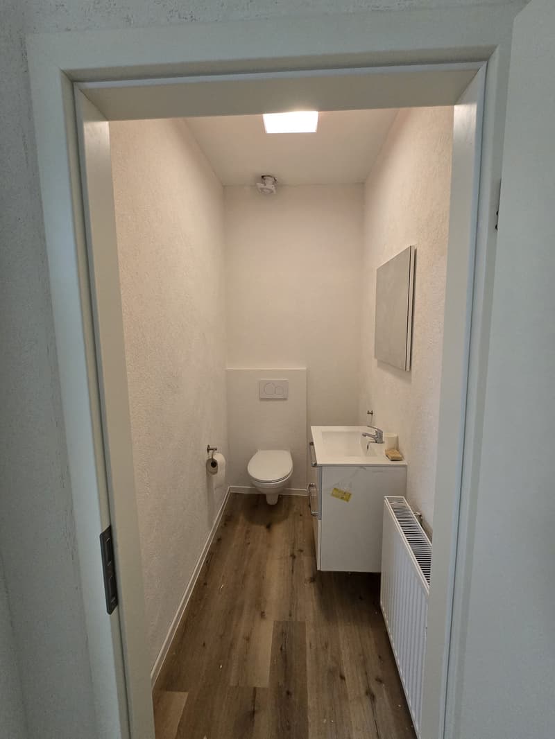 small bathroom with white tiled floor, white walls, white sink, white toilet, radiator, mirror