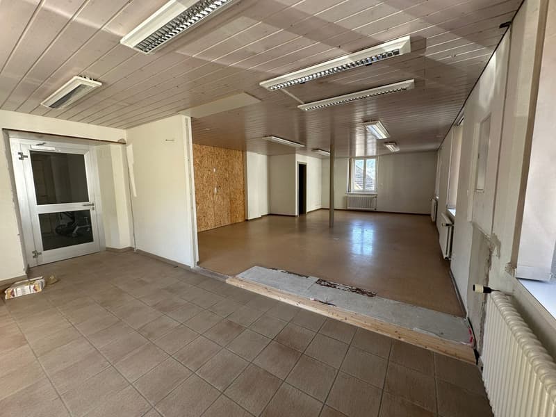 Empty room with tiled floor, white walls, wooden ceiling, and multiple windows.