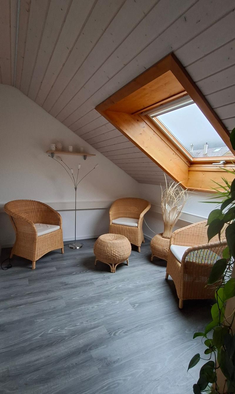 small attic room, hardwood floor, three wicker chairs, ottoman, coffee table, floor lamp, decorative plant, skylight