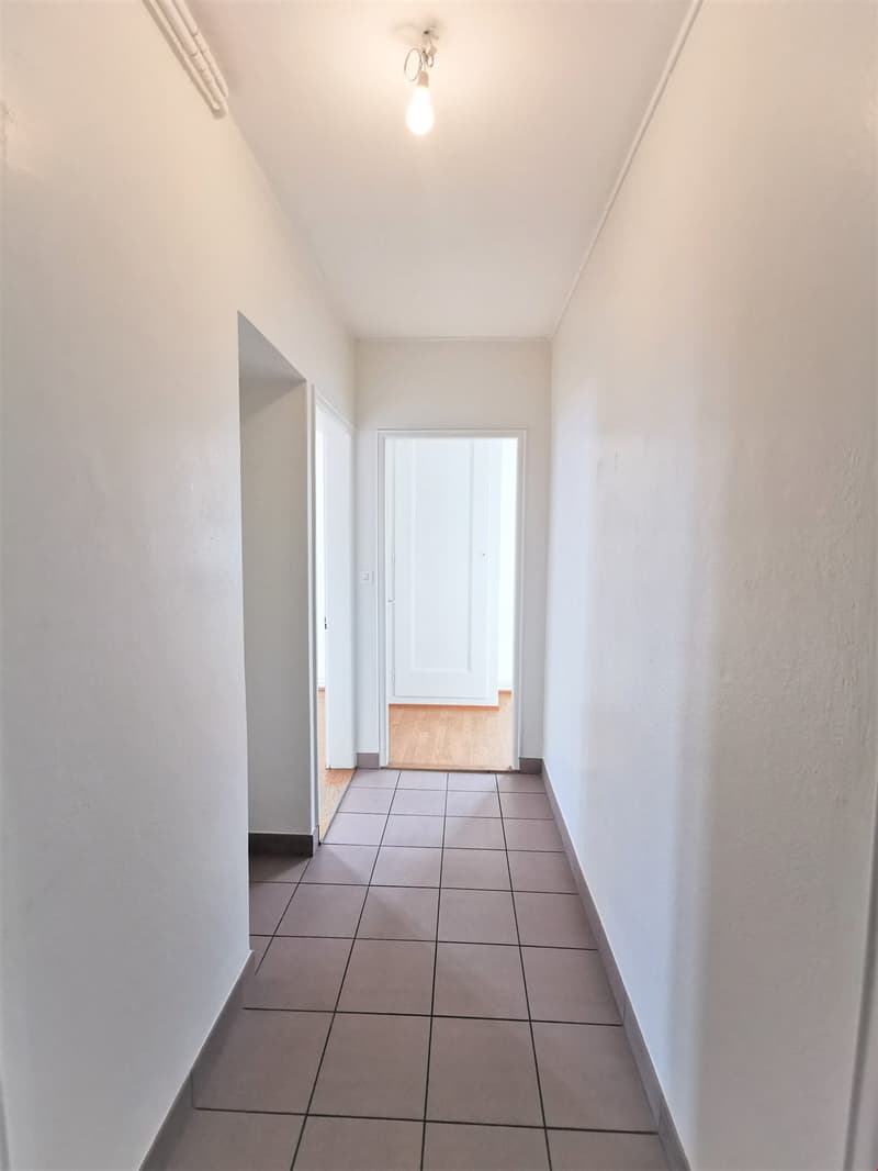 Empty corridor with tiled floor and white walls, wooden floor in the hallway, and a ceiling lamp.