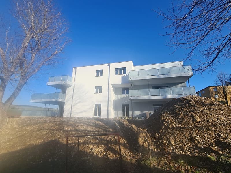 white building with balconies, multiple floors, windows, sunny day, pile of dirt in front