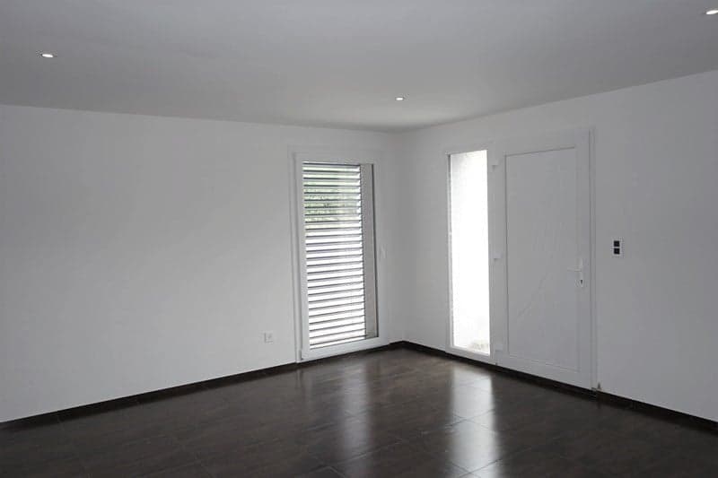 Empty room with white walls, wooden floor, white doors, white ceiling, glass door, and a window with shutters.