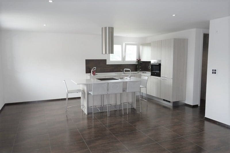 Modern open plan kitchen with island, white cabinets, tiled flooring, center sink, oven, built-in extractor, refrigerator