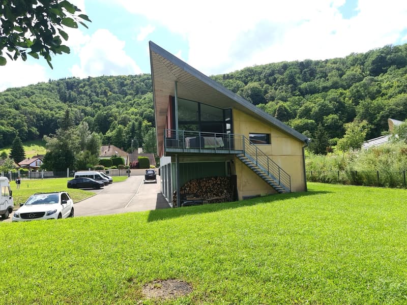 Modern house, yellow facade, gray roof, glass wall, garage, balcony, green surroundings, fenced area