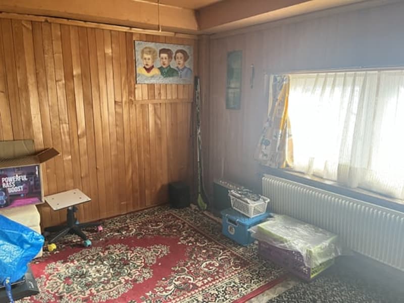 Wooden paneled walls, floral patterned rug, curtains, and various personal items and furniture such as a bed, dresser, and shelves with decorative items.