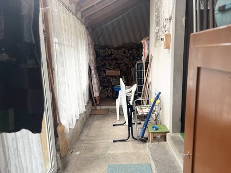 Narrow hallway with wooden beams, stacked firewood, and various storage items and tools