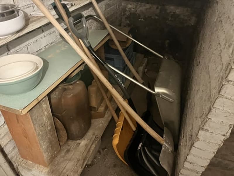 The image shows a cluttered basement or storage area with various items such as buckets, tools, and other miscellaneous objects stored on shelves and the floor.