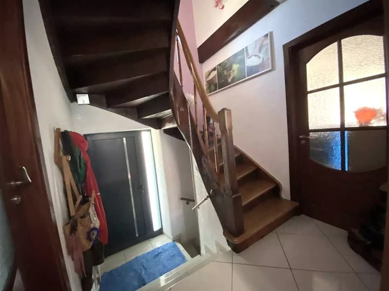 Entrance with a wooden staircase, beige handrail, and tiled flooring.