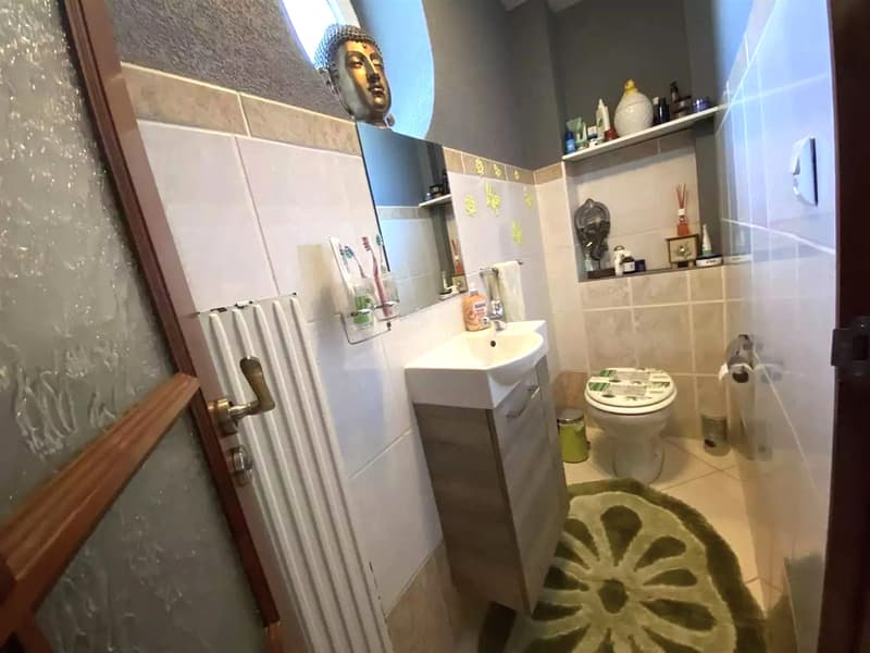 modern bathroom with a sink, mirror, toilet, and shelf; white tiled walls; green mat; radiator mounted on the wall