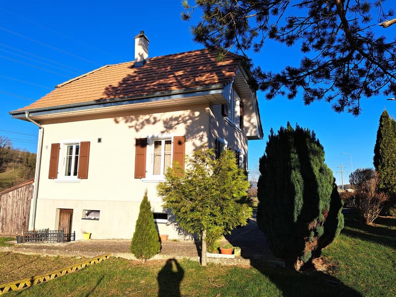 2 story house, beige walls, brown roof, brown window shutters, fenced yard, trees, small garden, chimney