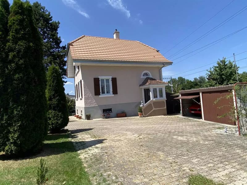single story house, brown tile roof, beige and white walls, chimney, garage, driveway, multiple potted plants, greenery