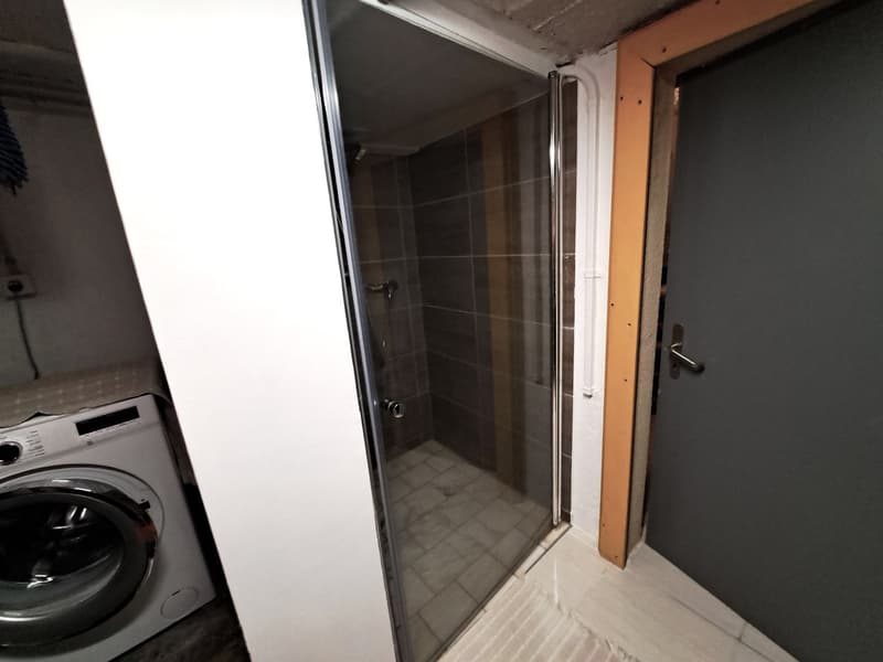Small space with a washing machine on the left, a shower with tiled walls, and an entrance door on the right