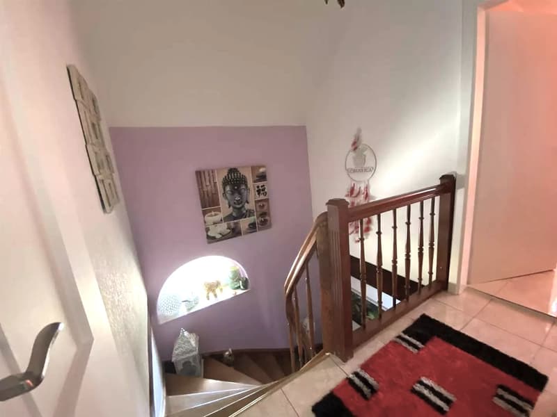 Wooden staircase, pink wall, Buddha picture, window with decorations, red carpet at the bottom